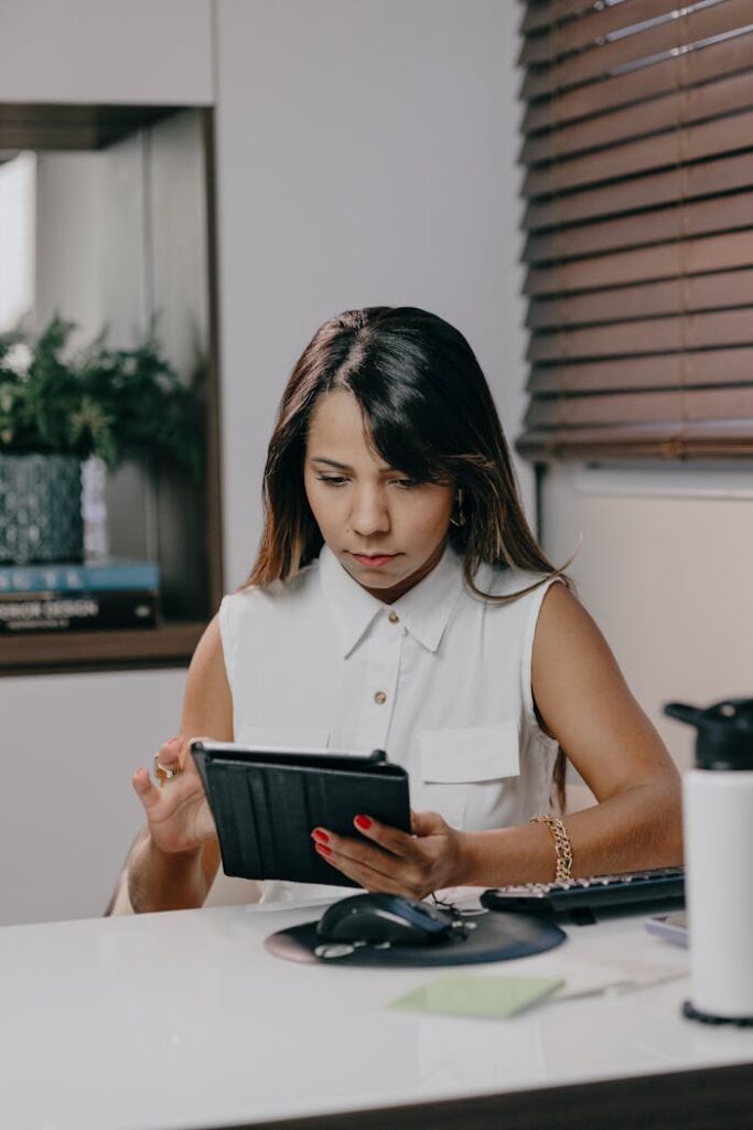 pexels photo 17489831 Confident adult woman in white shirt using tablet at office desk with focused expression.